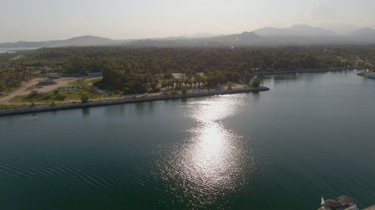 Wide drone view of calm water, ripples, shoreline palms, and mountains