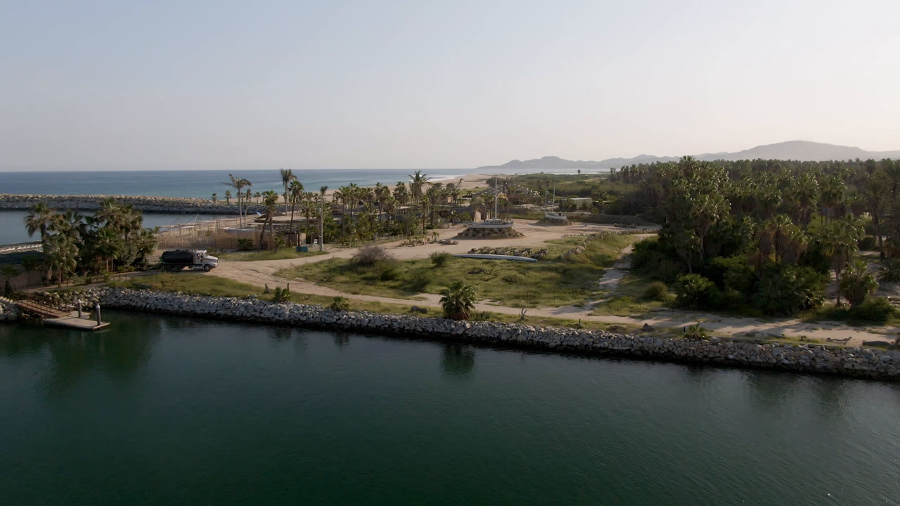 Elevated coastal view with inlet water, low island greenery, palms, and distant hills.