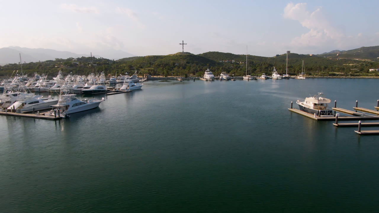 Puerto Los Cabos marina aerial showing a cluster of yachts left of center, a small docked boat in the foreground area, hills along the shore, and no visible people.