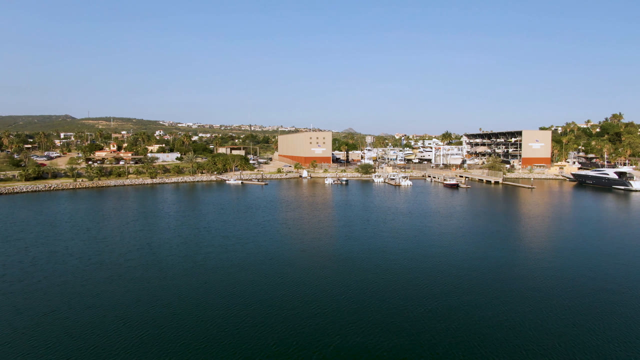 Aerial marina scene with a large yacht at right, small boats near docks, and buildings along shore.