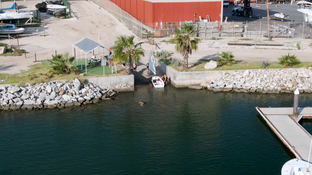Overhead marina water with dock corner in the foreground and a small boat at the shoreline ramp.