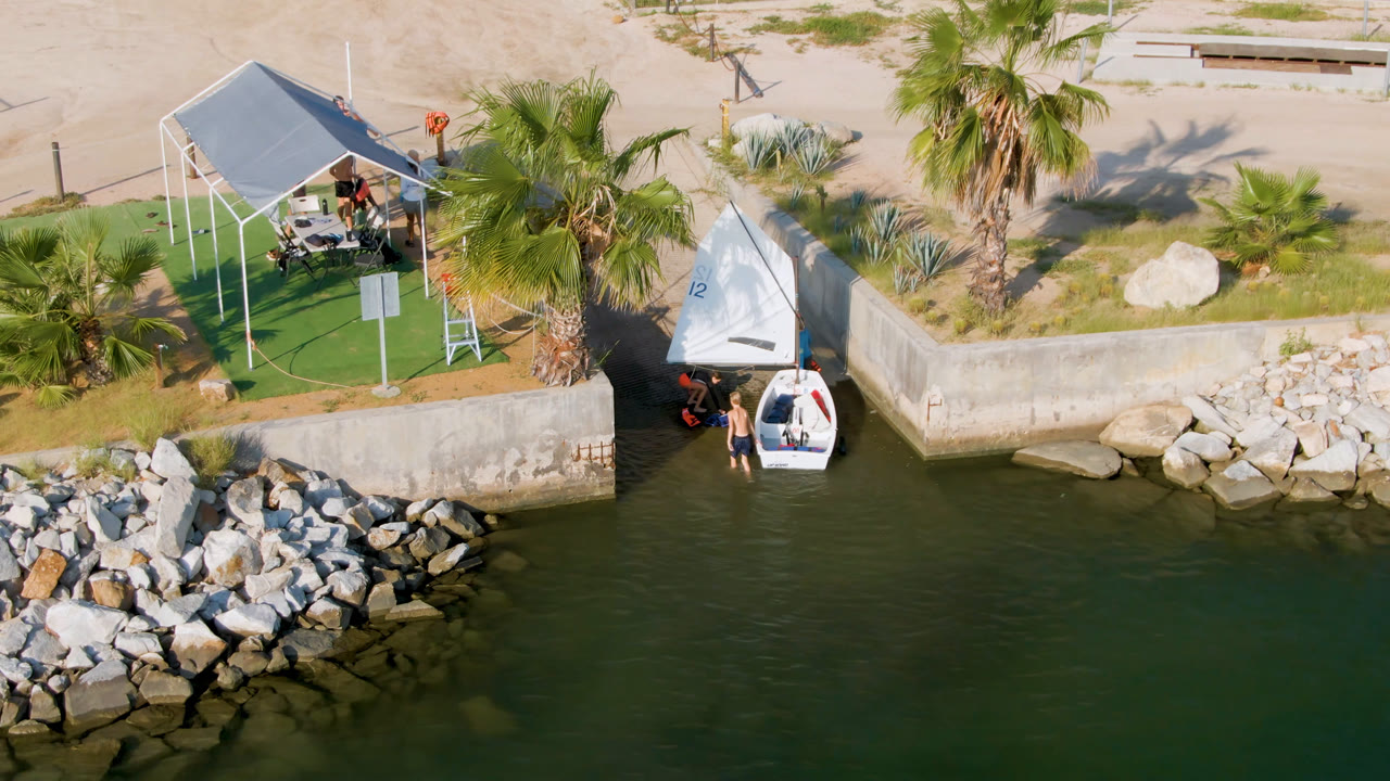 Overhead view of a small boat beside a seawall near palms and a shade structure.