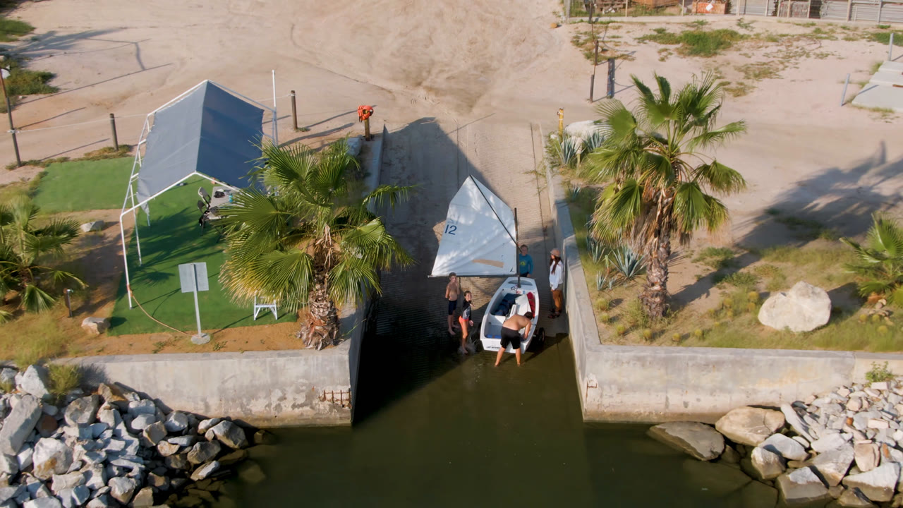 Overhead view of a small sailboat beside a canal wall and palms.