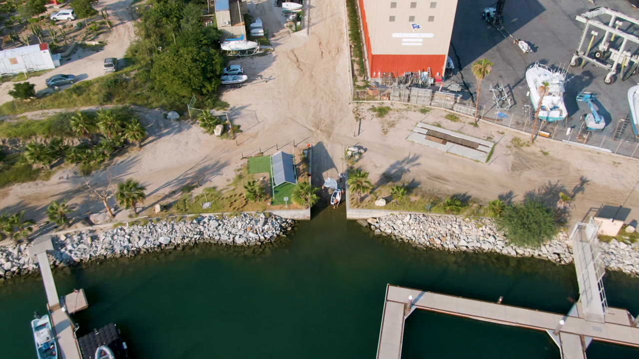 Overhead harbor water, docks, shoreline rocks, boats, road, and buildings.