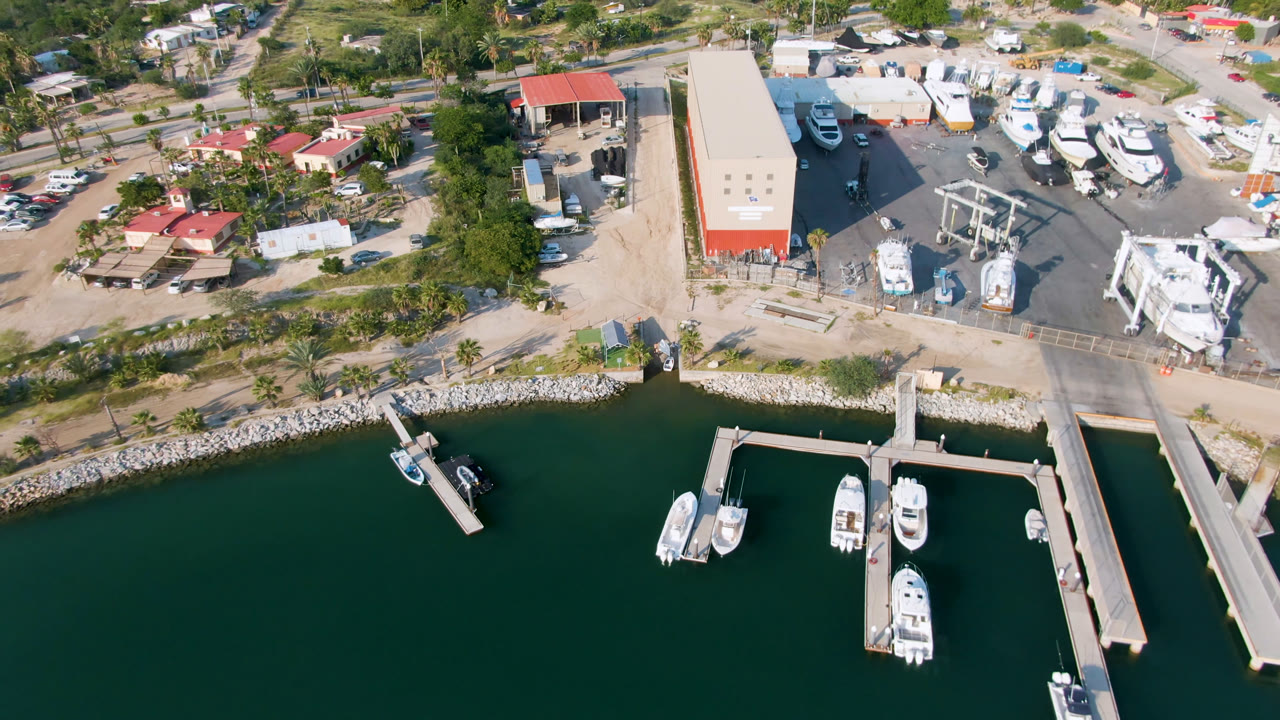 Birdseye view of marina docks, boats, a bridge approach, and shoreline buildings.