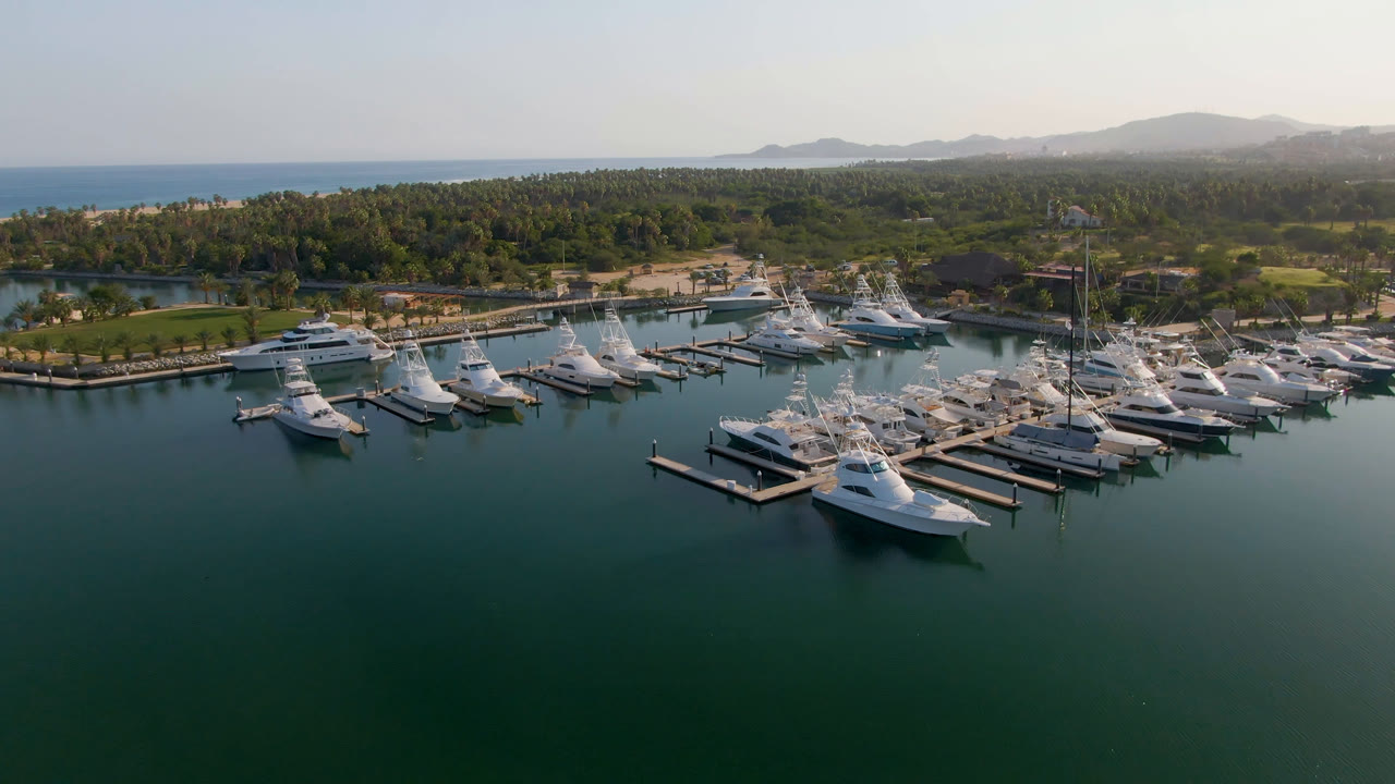 Aerial marina scene with boats moored beside docks and coastal hills behind.