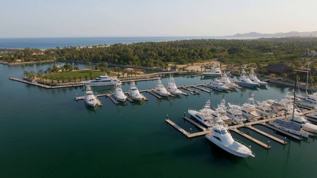 High aerial marina scene with yachts, docks, a small island, and distant hills