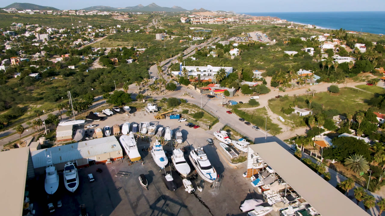 Aerial view of boats parked in a lot near roads, buildings, hills, and ocean.