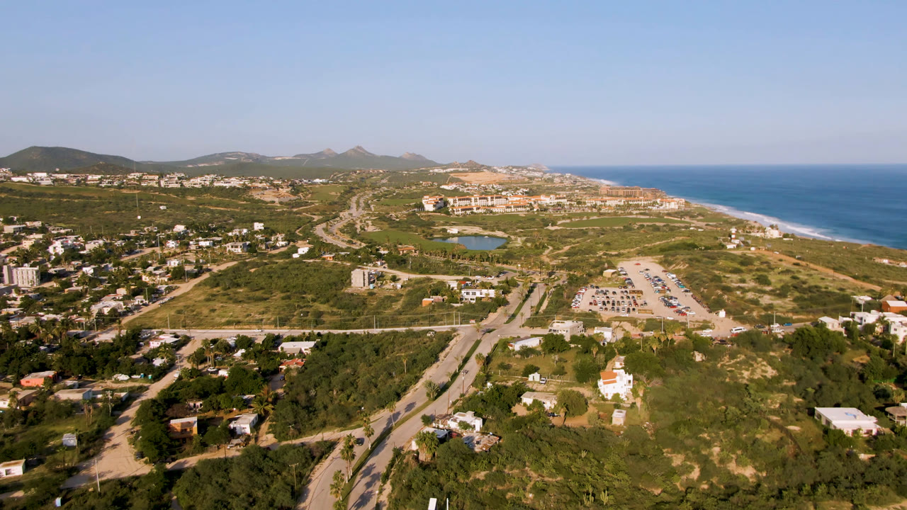Wide aerial view of coastal roads, homes, lagoon, beach, ocean, and hills.