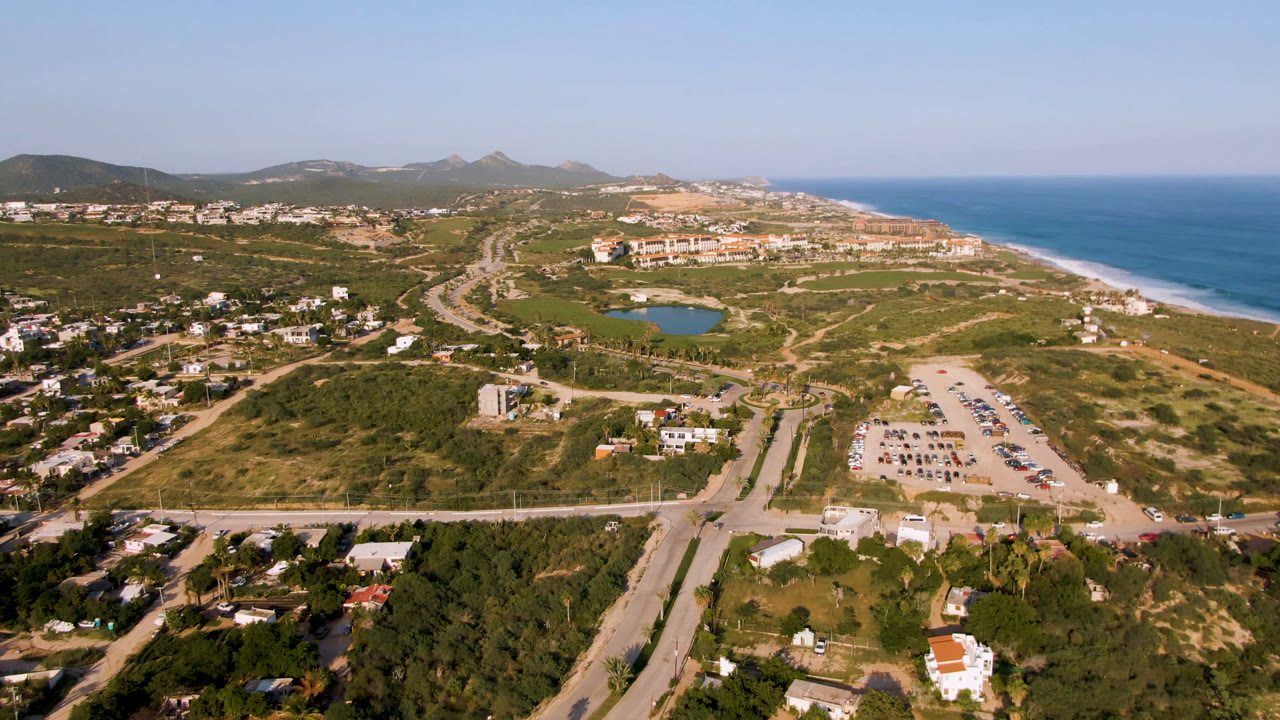 Aerial view of coastal roads, green terrain, beach, ocean, and distant hills
