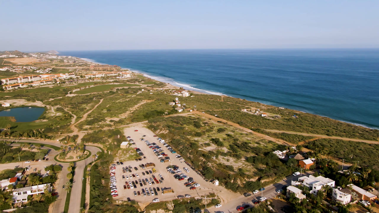 Aerial view of beach, ocean, parking lot, roads, and coastal buildings.