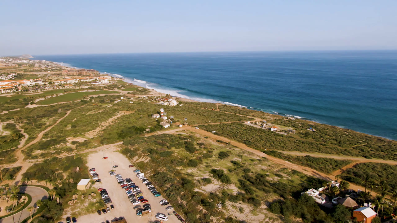 Aerial coastline with beach parking, dirt roads, dunes, and blue ocean.