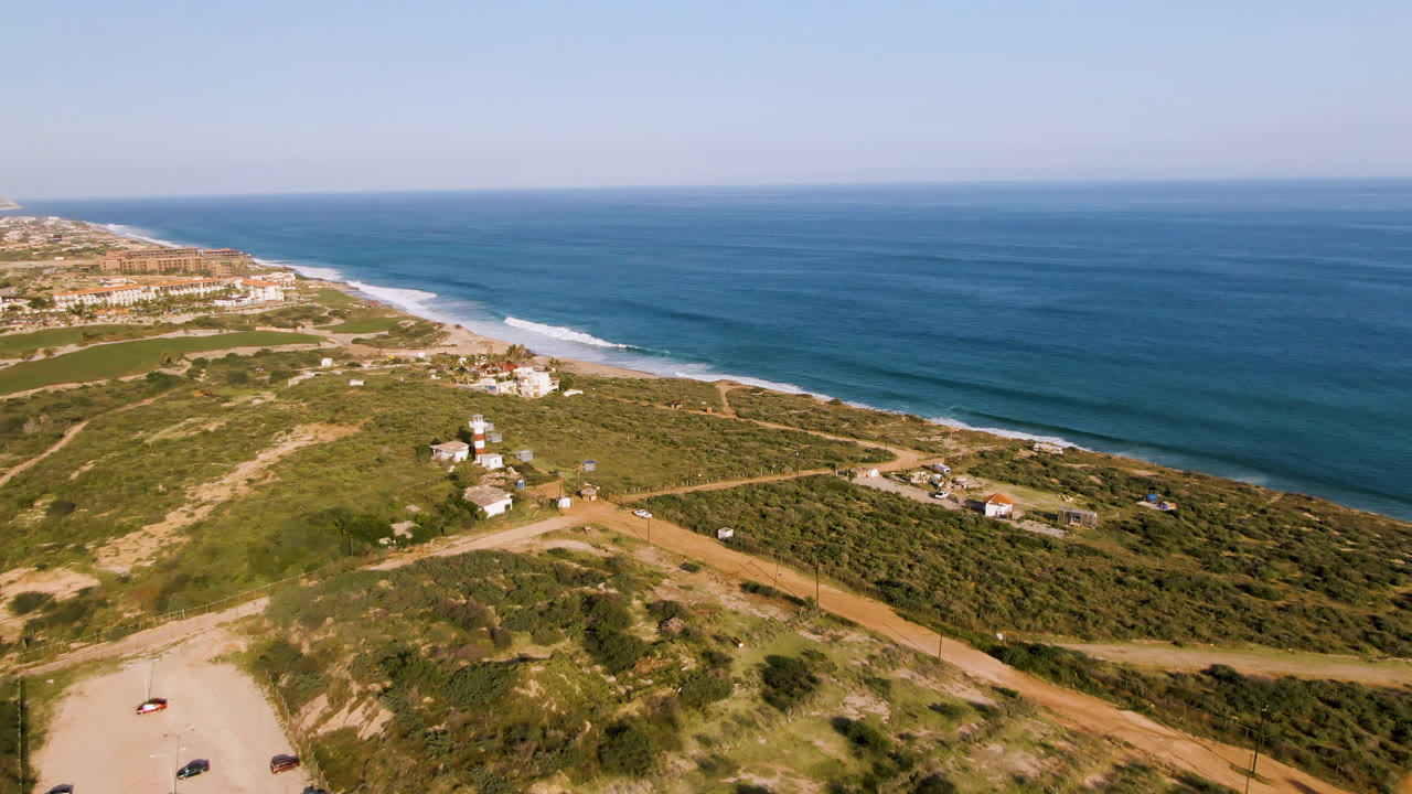 Drone view of coastal scrubland, dirt roads, beach, and blue ocean.