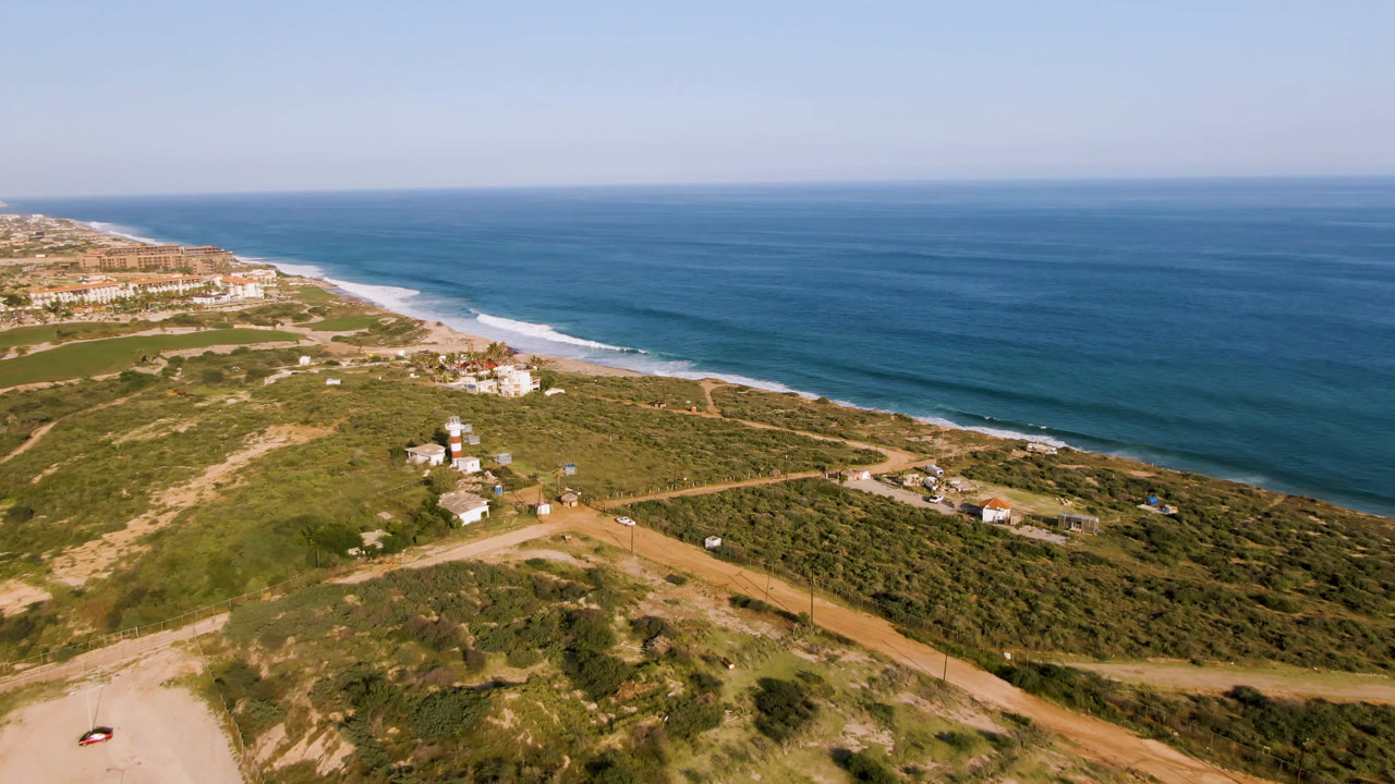 Aerial view in Puerto Los Cabos with the shoreline running diagonally past scrubland roads, scattered buildings, and no visible people.