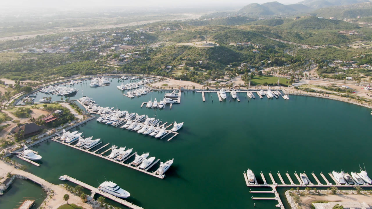 Wide drone view of a marina basin with docked boats and coastal development beyond.