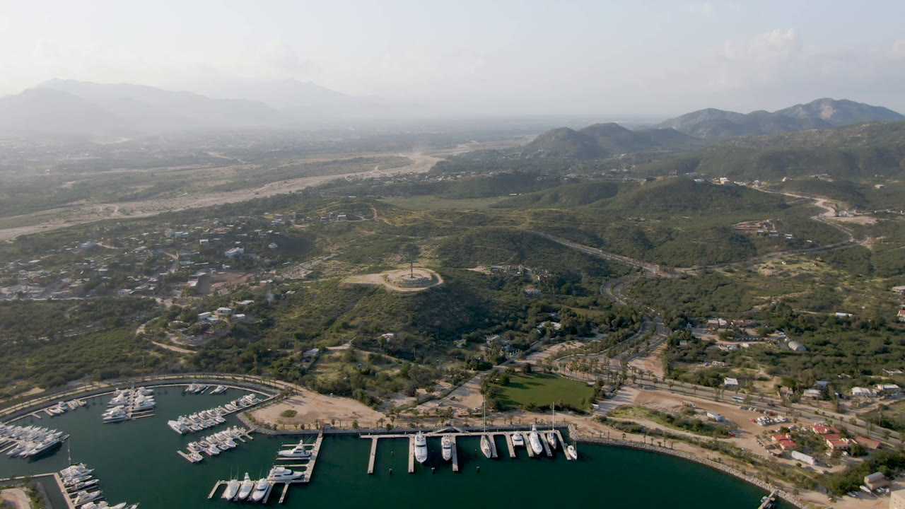 Drone view of marina docks with coastal hills, buildings, and mountain horizon