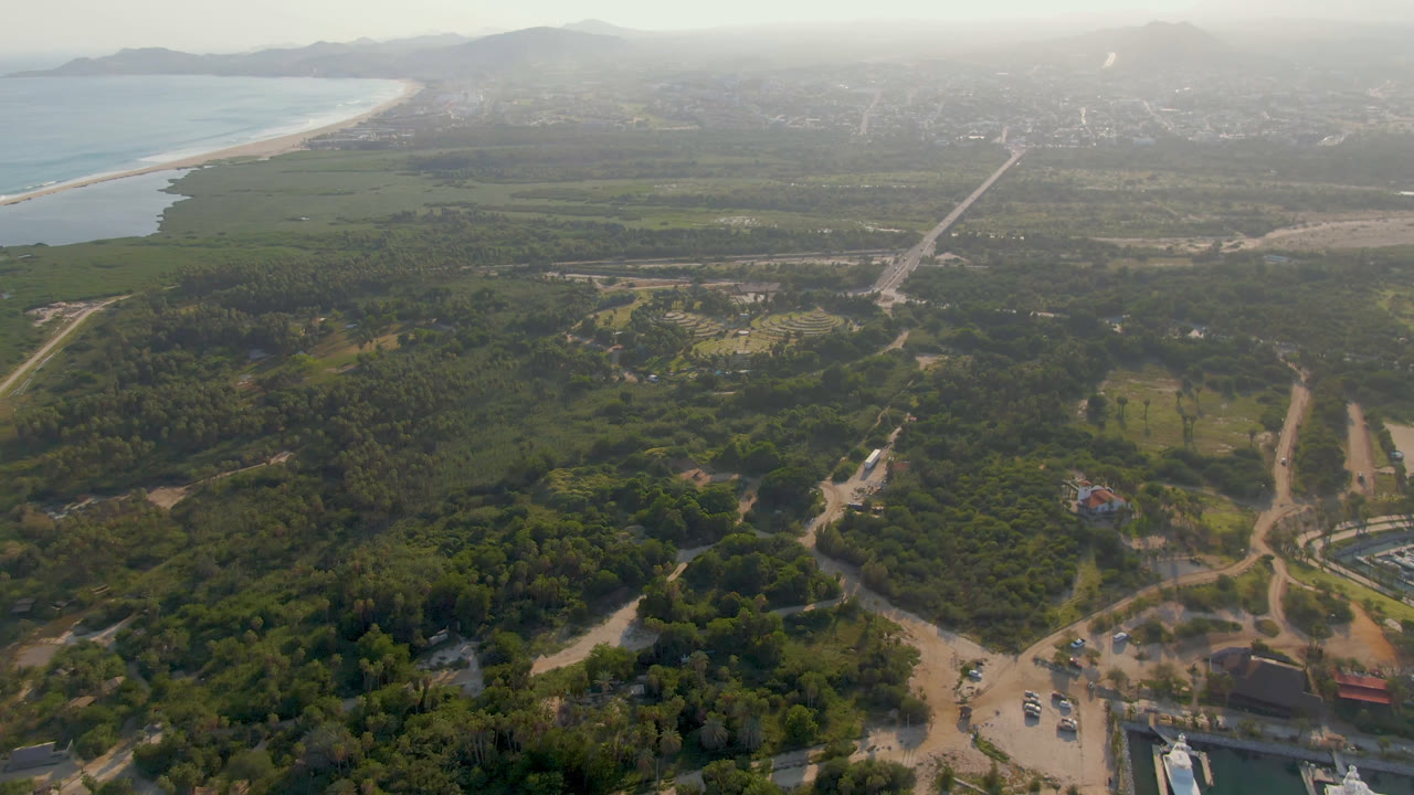 High drone view of beach, ocean, green land, roads, and distant mountains.