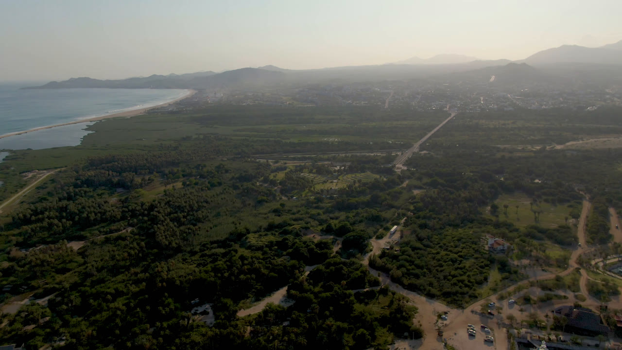 High aerial view of coastline, green terrain, roads, and distant mountains.