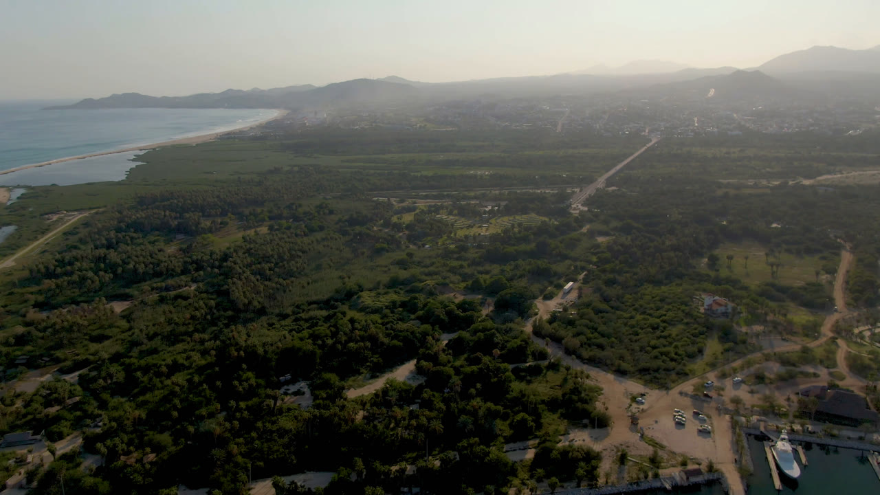 High aerial view of coastline, green land, roads, marina water, and distant mountains.