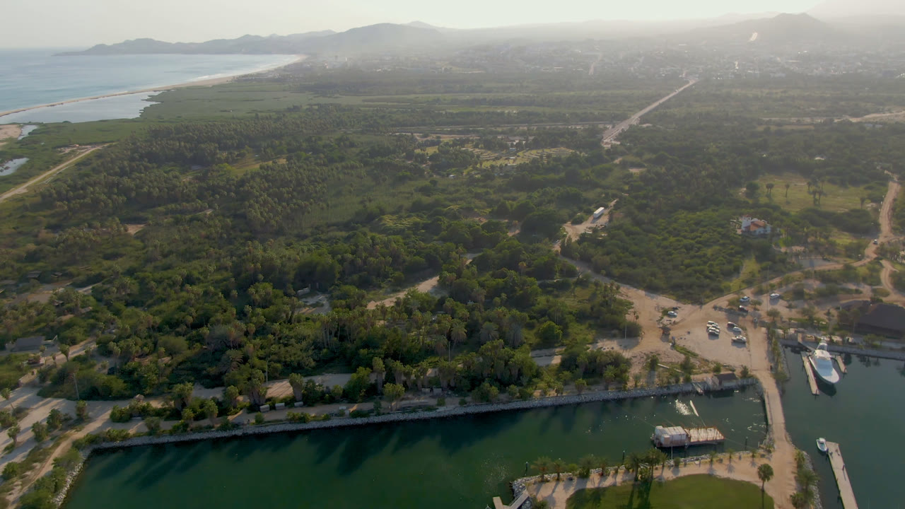 Aerial view of docked boats, marina basin, wooded land, roads, ocean, and hazy hills.