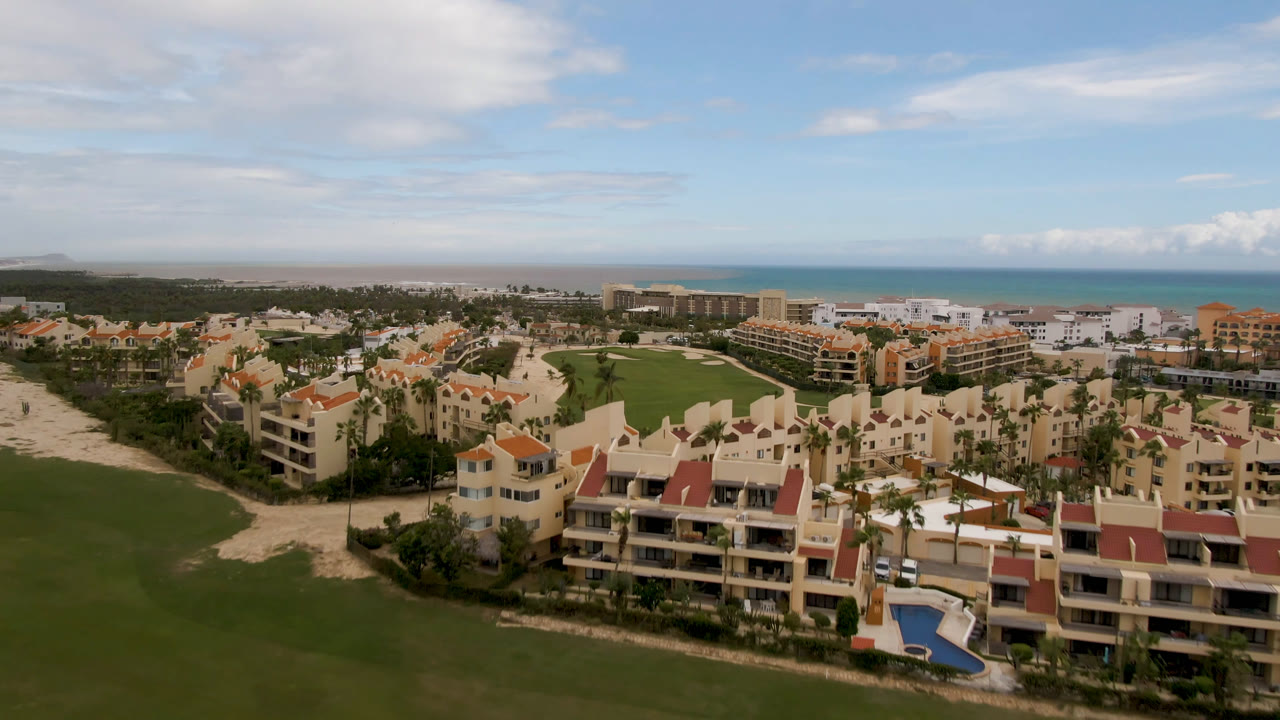 Wide aerial of resort roofs, golf green, palm trees, and blue ocean.