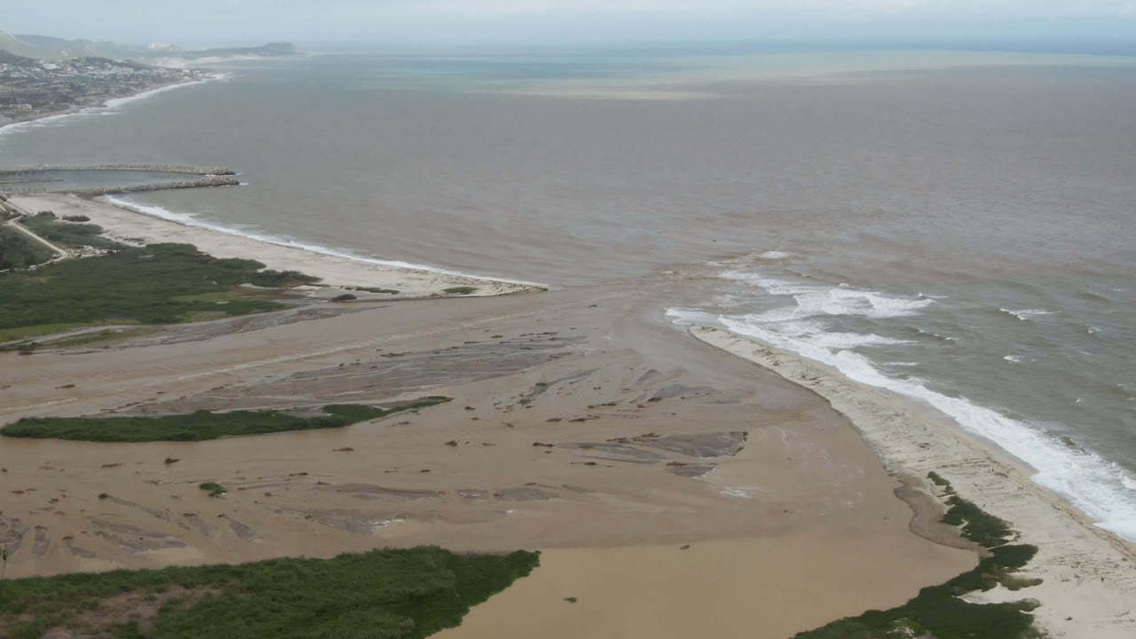 Wide aerial beach view with sand flats, ocean, surf, and distant coast.
