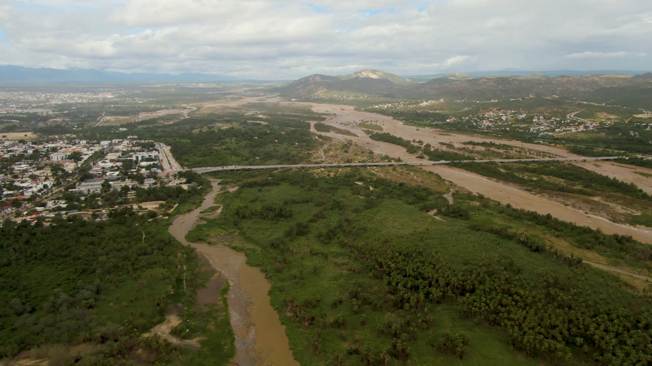 High aerial shot of a green river valley, nearby roads, town buildings, and distant hills.