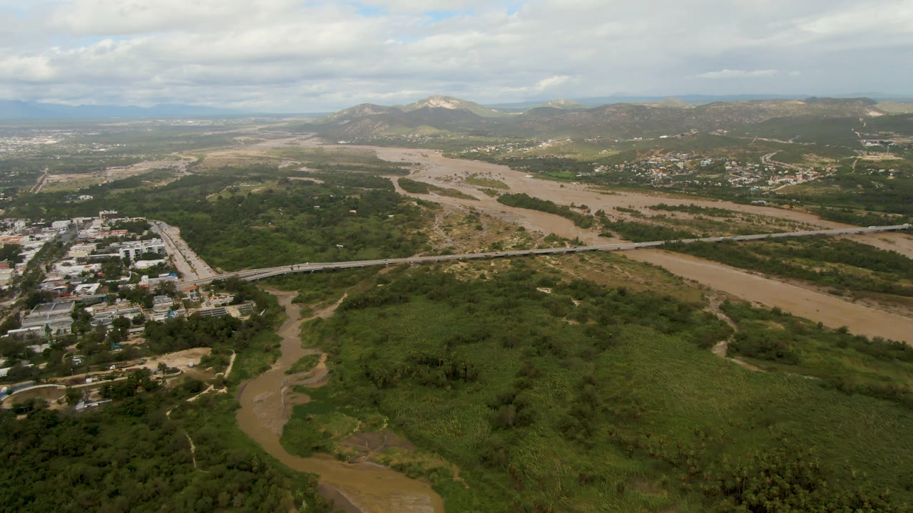 Aerial landscape with green valley, muddy river, scattered buildings, and mountains.
