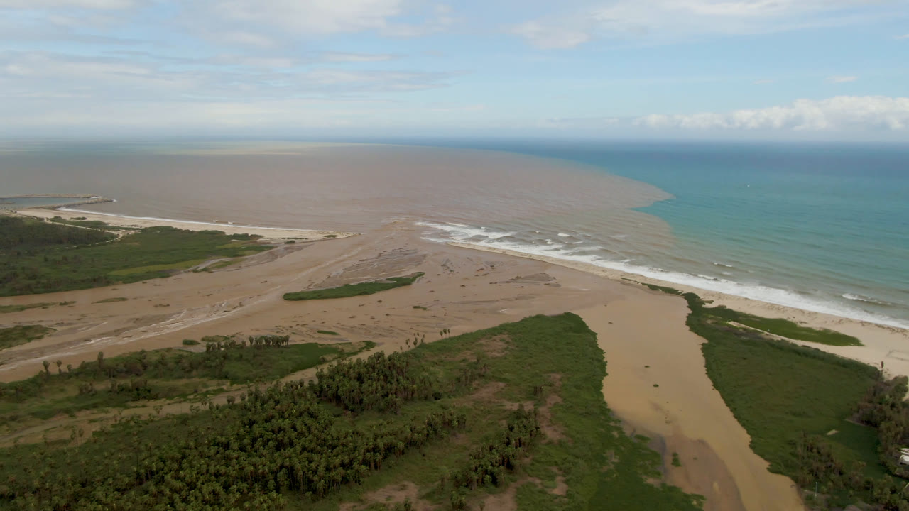 Wide aerial view of a river mouth crossing a sandy beach into the ocean