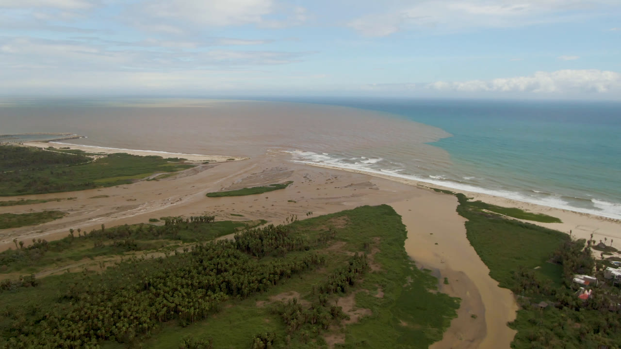 Wide aerial view of a sandy river mouth meeting ocean surf.