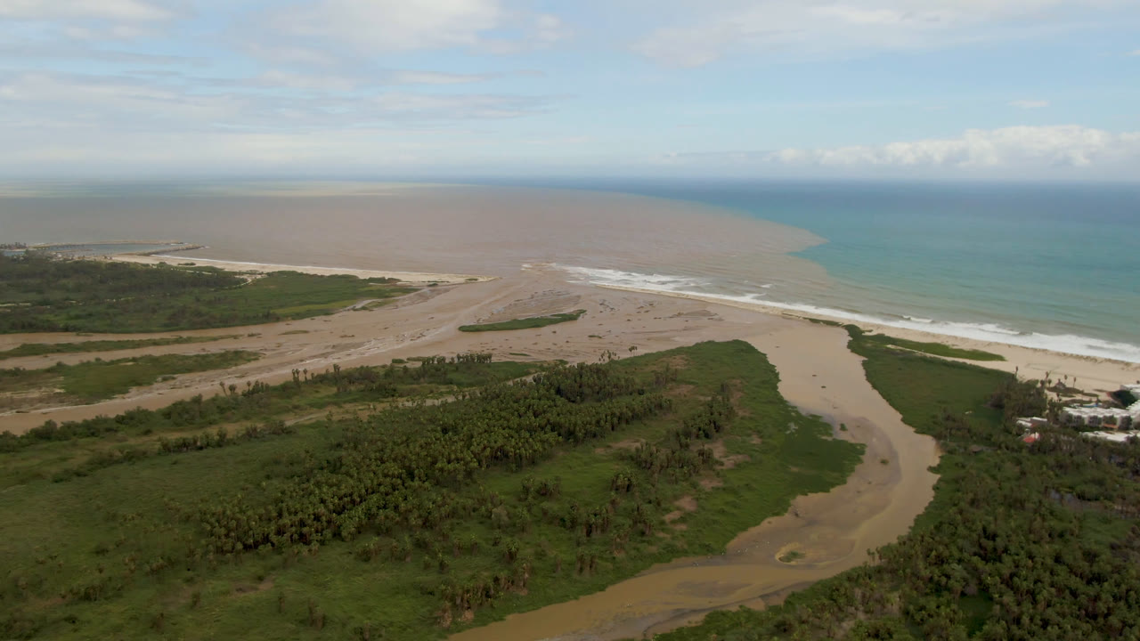 Aerial beach landscape with river water curving through vegetation toward blue ocean.