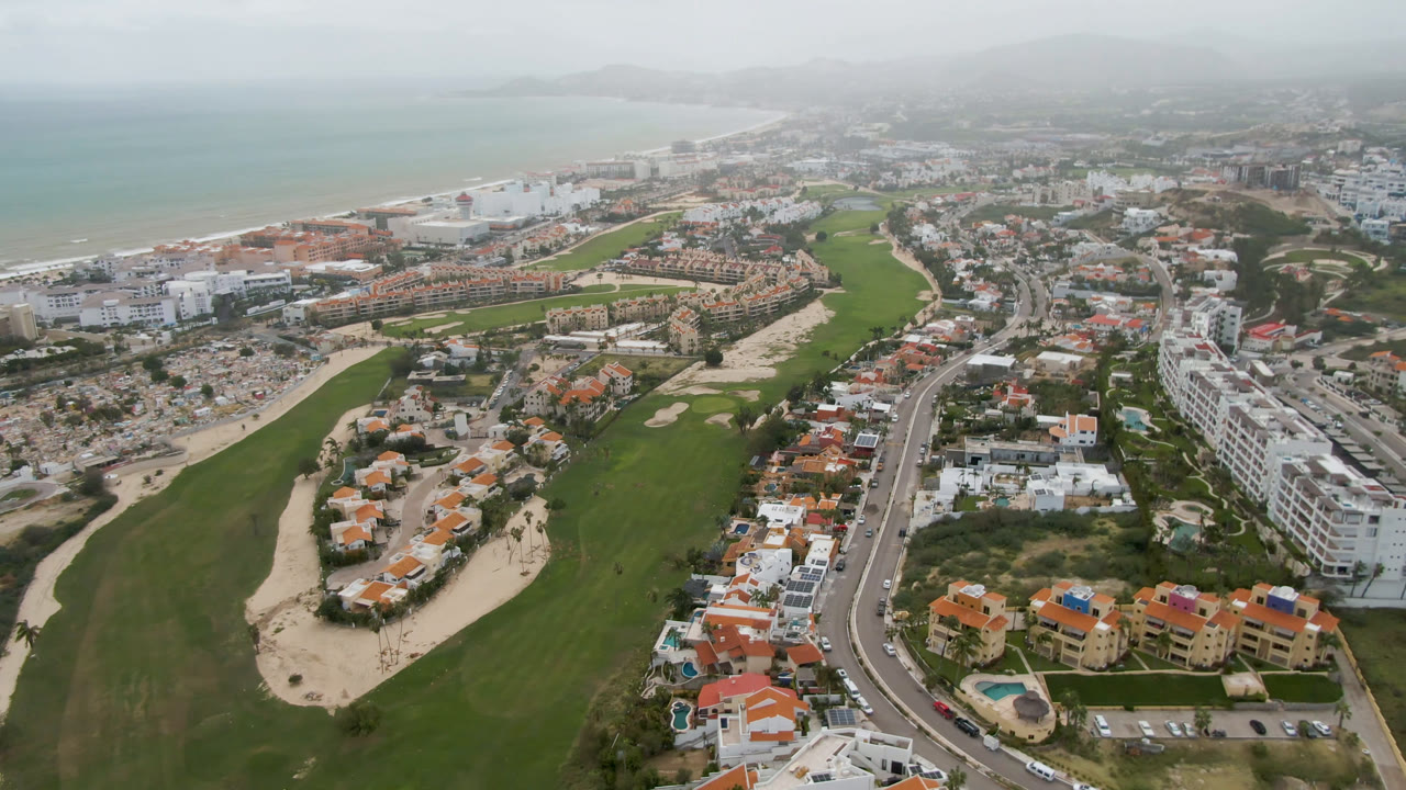 Wide aerial of coastal golf course and city beside hazy ocean