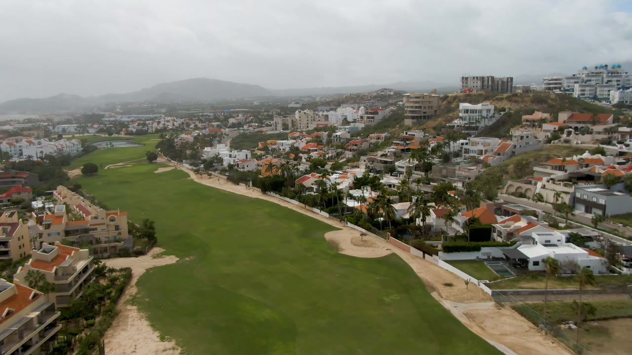 Golf course fairway bordered by homes and a road below a gray sky.
