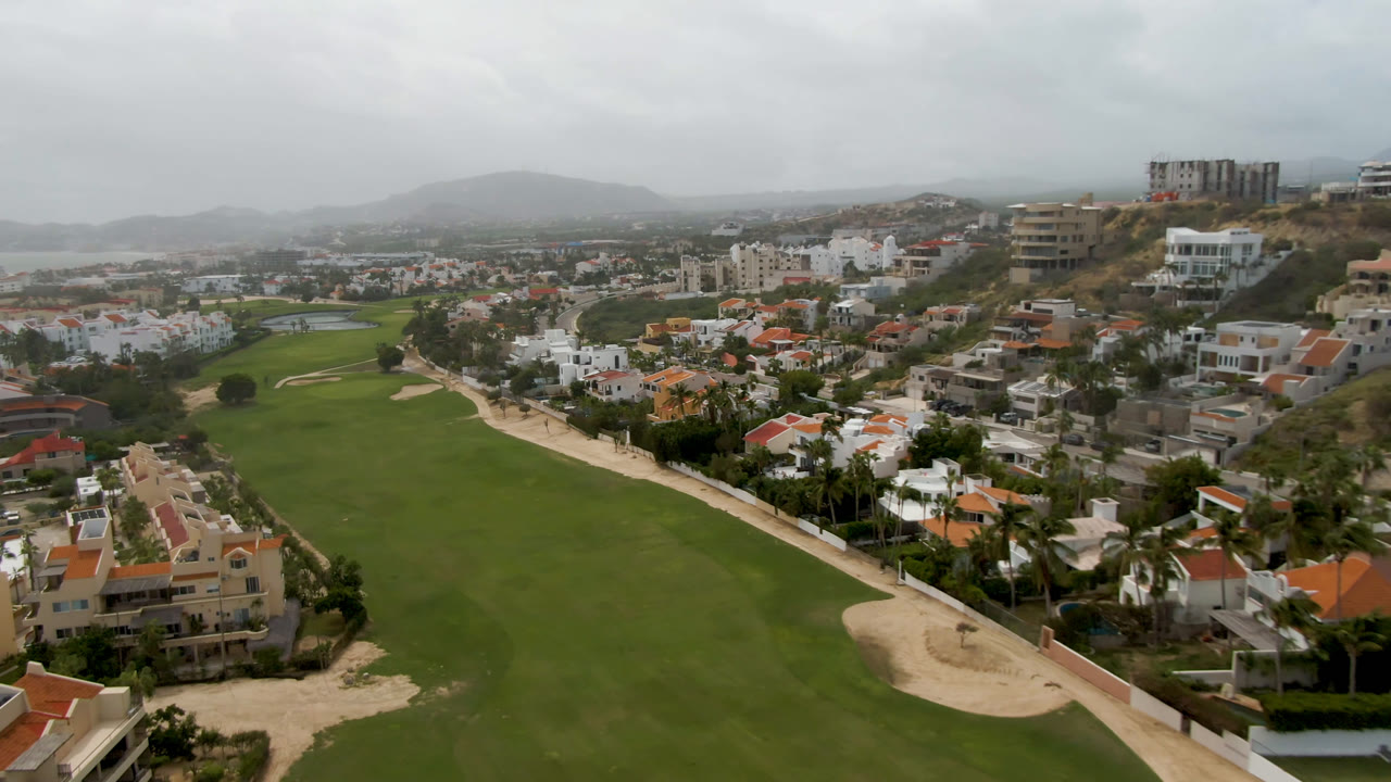 Aerial view of a golf course beside homes under cloudy sky.