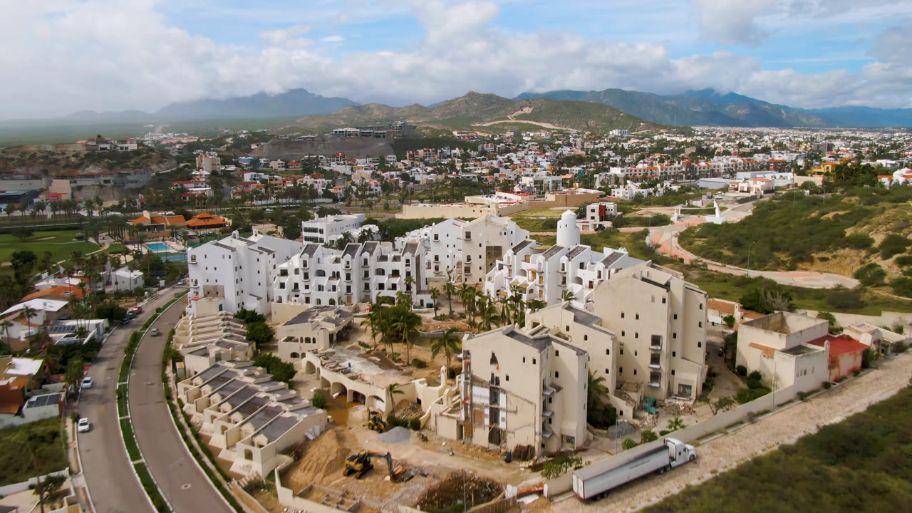 Aerial view of white buildings, roads, green terrain, and distant hills.