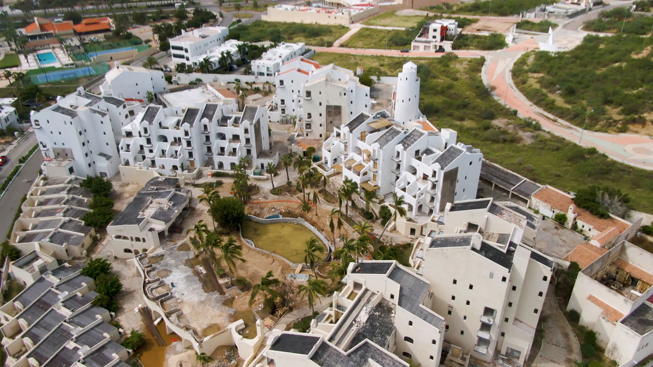Overhead view of white buildings around a small pond and palms