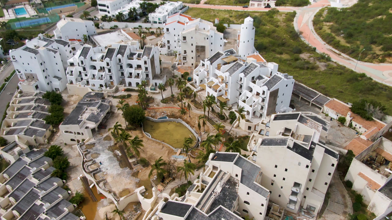 Aerial frame in San Jose del Cabo with the white building complex centered lower in the view, the small pond to the right, curving paths above, and no visible people.