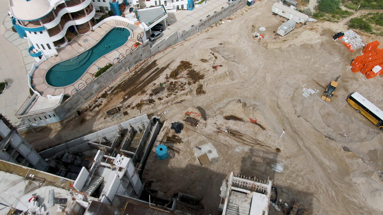 Construction site with pool, dirt lot, equipment, and bus from above.