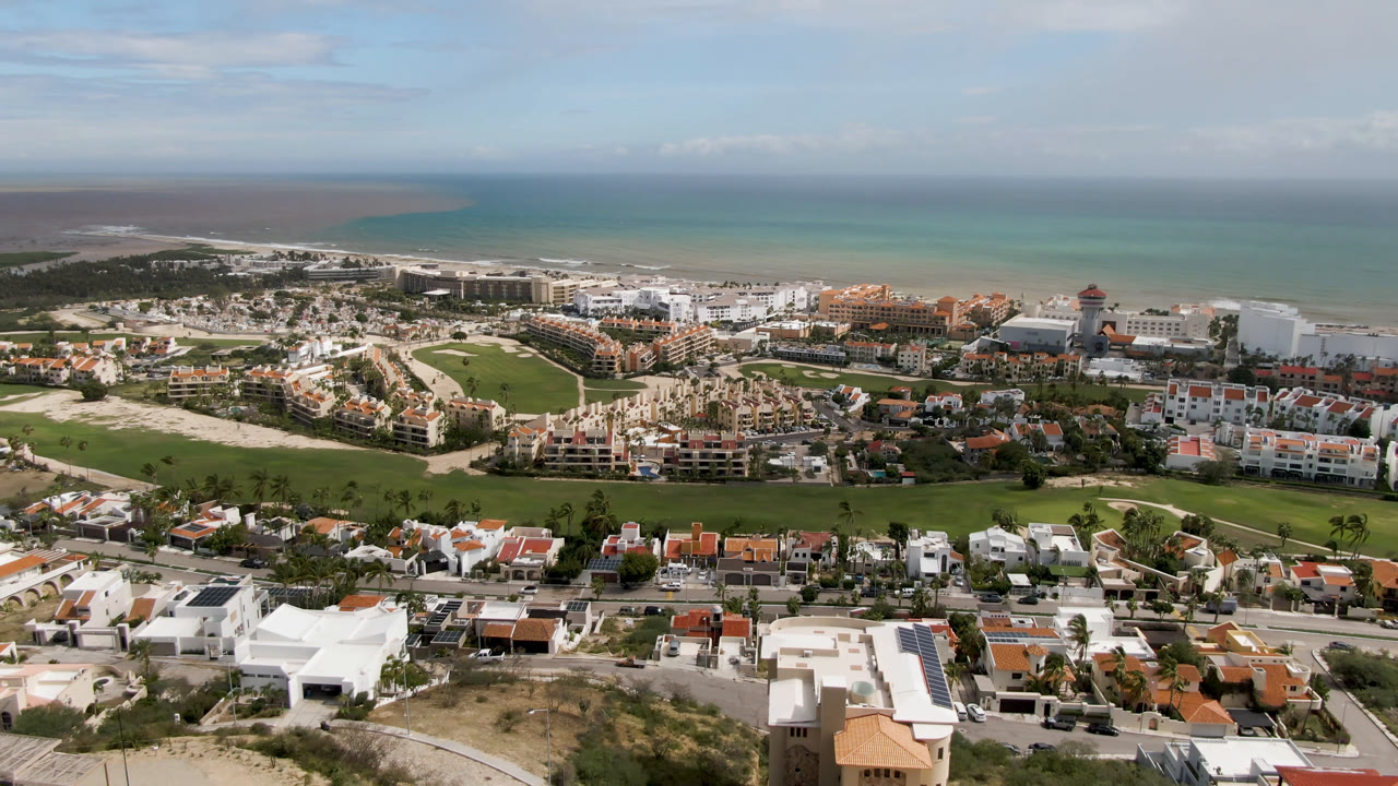 Wide aerial view of coastal resort buildings, golf greens, villas, and ocean horizon.