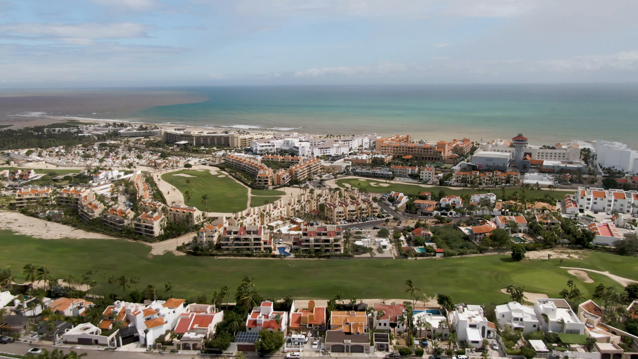 Drone view of resort coastline, golf greens, beach, and ocean horizon.