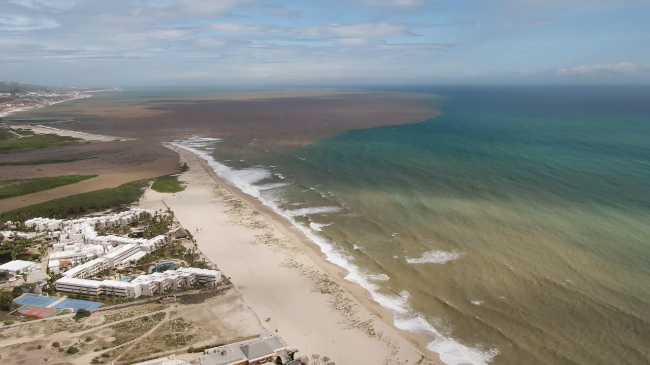 Drone view of beach resort, sand, surf, and open water.