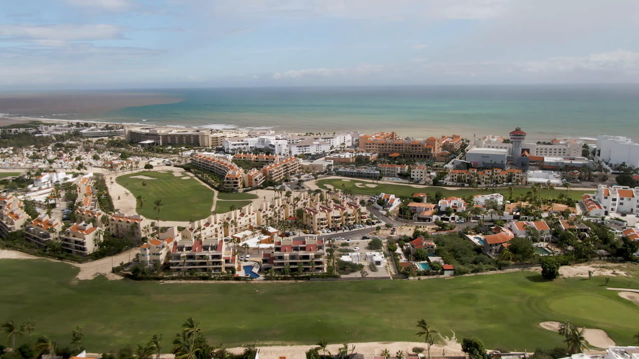 Wide aerial view of golf fairways, resort buildings, and ocean horizon