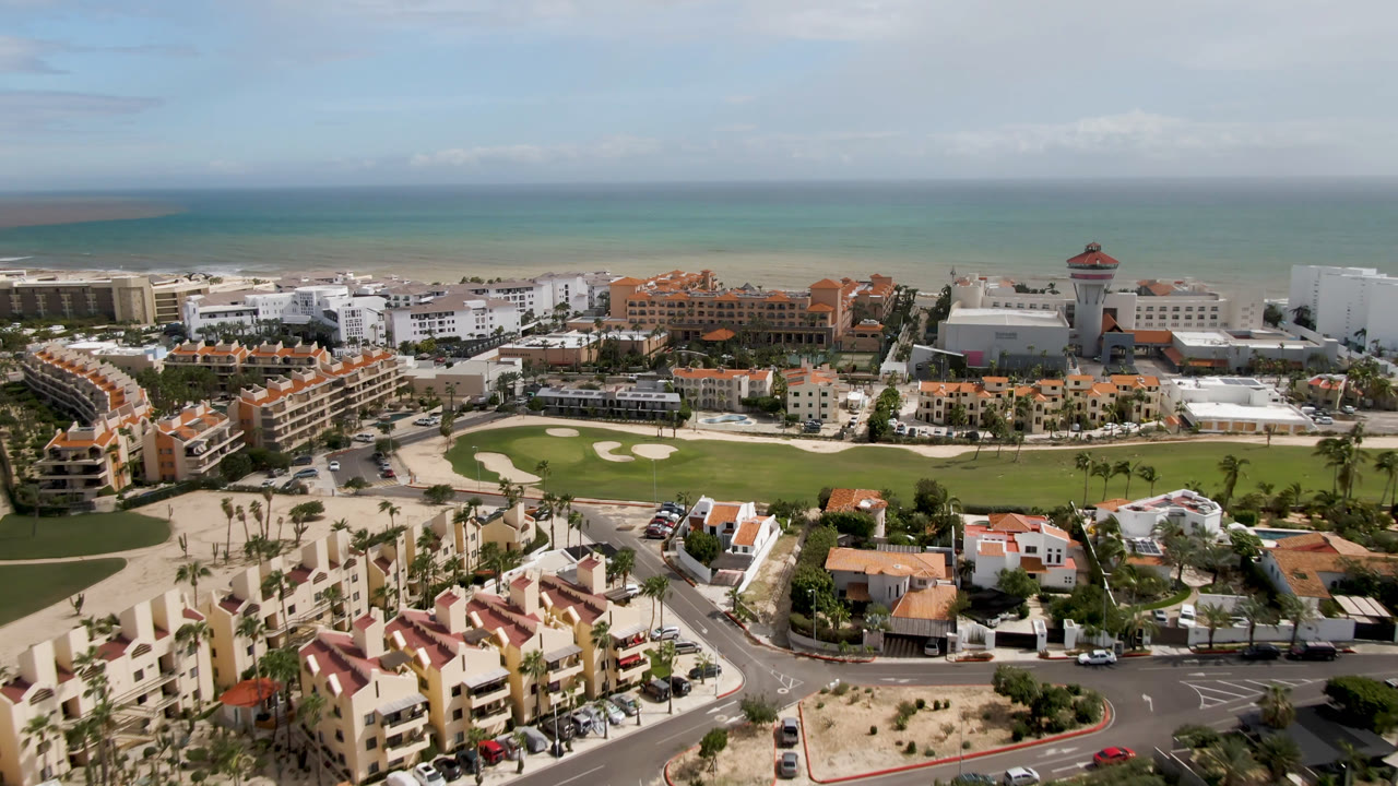 Aerial coastal city view with golf course, buildings, beach, and ocean.
