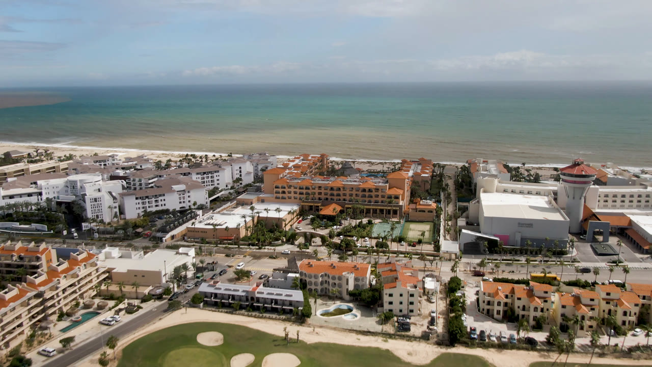 Drone-height view of resort buildings, beach, ocean, and golf course foreground.