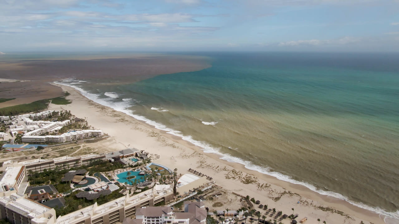 High aerial of beachfront hotel complex and shallow coastal water.