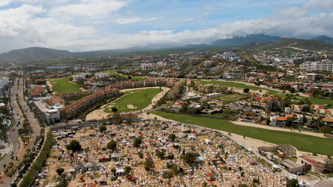 Aerial view of cemetery, golf course, roads, buildings, and mountains.