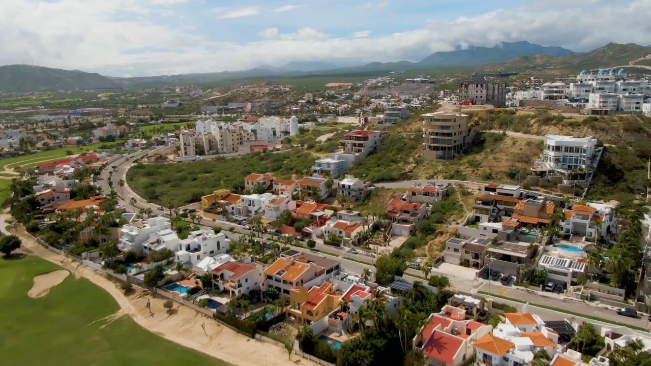 Aerial view of hillside homes, roads, golf grass, and distant mountains.