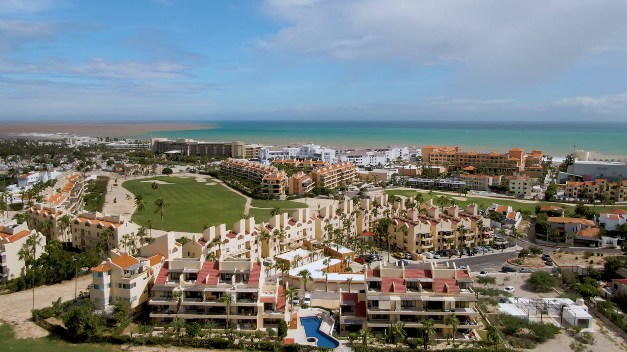 Drone-like aerial of beach resort, golf course, and blue water