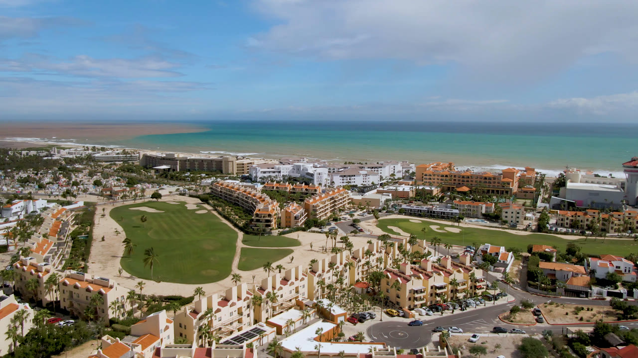 Second aerial frame in San Jose del Cabo showing the golf course more centrally, with white and orange buildings near the beach and no visible people.