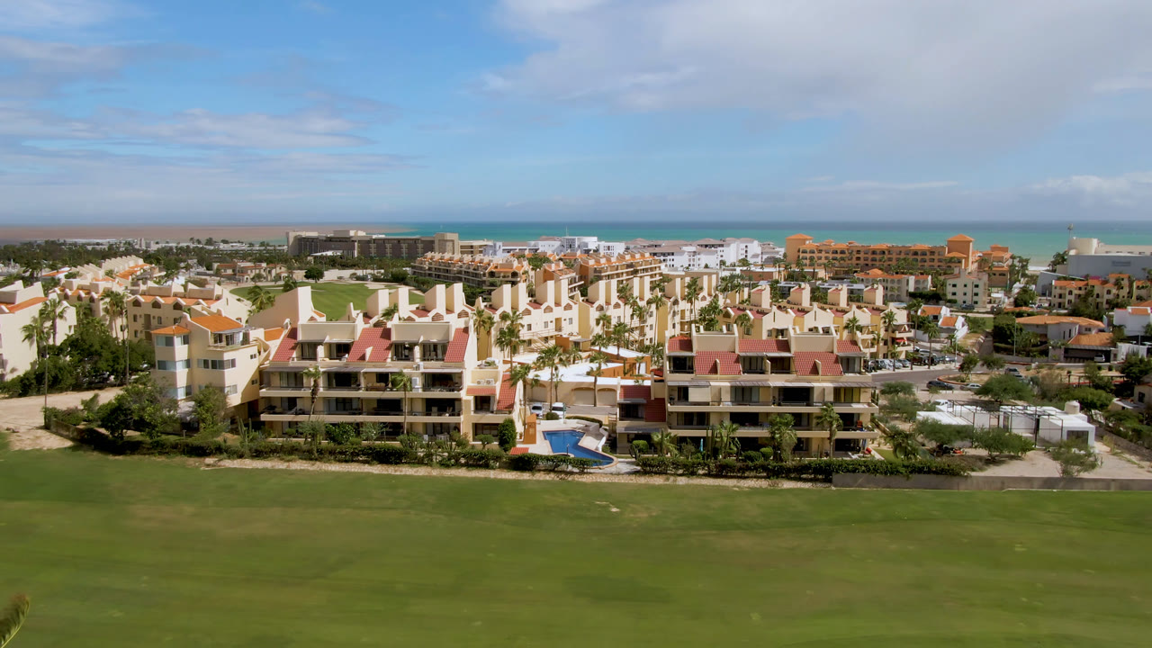 Wide elevated view of a golf course, residential buildings, and ocean horizon.